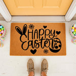 Happy Easter coir doormat featuring black bunny ears and egg design on a natural fiber welcome mat, perfect for spring porch decor with colorful baskets of eggs placed on a white floor in front of a yellow door for seasonal home