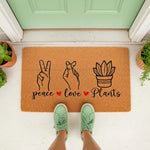 Peace Love Plants doormat featuring hand signs and a potted succulent design on natural coir fiber, perfect for a front porch welcome mat or housewarming decor for plant lovers who enjoy botanical home entryways and garden style.