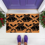 Christmas bell pattern coir doormat featuring black holiday bells and holly leaves on a natural fiber welcome mat, placed on a white porch in front of a purple door for festive seasonal home decor and entryway floor protection.