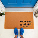 Personalized Mr. and Mrs. wedding doormat for a new home, featuring a custom last name and established year on a natural coir welcome mat, perfect for a newlywed couple gift or housewarming decor at a front door entrance.