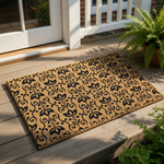 Floral pattern coir doormat featuring a black scrollwork design on natural tan fiber, placed on a wood porch as a stylish outdoor welcome mat for home entryways, front door decor, and patio floor covering for a modern farmhouse
