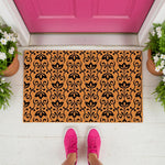 Floral pattern coir doormat featuring a black botanical print on natural fiber, displayed as a stylish front porch welcome mat in front of a bright pink door with potted white flowers and a person wearing pink sneakers standing