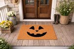 Jack-o-lantern pumpkin face doormat for fall porch decor, featuring a natural coir welcome mat with a black carved pumpkin design on a rustic wood front porch setting with seasonal flowers and boots for autumn home entryway style.