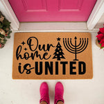 Holiday welcome doormat featuring a Christmas tree and menorah design with the text Our home is UNITED, a natural coir fiber floor mat for front porch decor that celebrates winter seasonal traditions and festive home entryways.