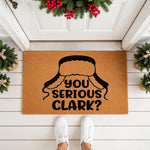 Funny winter holiday doormat featuring a black trapper hat graphic and the text You Serious Clark, this natural coir welcome mat is a festive front porch decor piece for Christmas home entryways and seasonal outdoor floor mats.