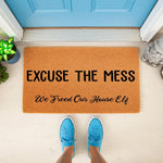 Funny doormat with the text Excuse the Mess We Freed Our House Elf, a natural coir welcome mat for front porch decor that makes a humorous housewarming gift for fantasy fans and home entryway floor mat enthusiasts.