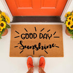Good Day Sunshine coir doormat featuring a cheerful typography design on a natural fiber welcome mat, placed at a bright orange front door with sunflowers, perfect for a modern porch entry or a housewarming home decor gift.