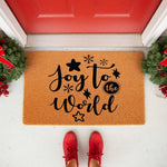 Joy to the World Christmas doormat featuring black text and snowflake star designs on a natural coir fiber welcome mat, placed at a red front door with holiday wreaths for festive seasonal home decor and entryway floor mat
