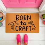 Born to Craft doormat for crafters, featuring a glue gun and scissors design on a natural coir welcome mat, perfect for a sewing room or craft studio entrance, shown on a porch with colorful yarn balls and bright pink shoes.