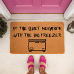 Funny doormat with the text I am the quiet neighbor with the big freezer and a chest freezer icon, this natural coir welcome mat is a humorous front porch decor piece for true crime fans and dark humor home entryway styling.