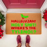 Funny Christmas doormat with red and green text reading Hallelujah Holy Shit Where's The Tylenol, featuring holly leaves on a natural coir welcome mat placed on a porch with festive holiday decor and a person wearing sneakers.