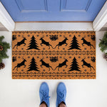 Christmas reindeer doormat featuring a festive pattern of black deer, pine trees, and bells on a natural coir welcome mat, perfect for holiday porch decor and winter entryway floor mats placed outside a blue front door.