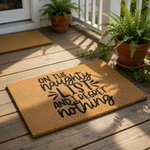 Funny Christmas doormat featuring the text On The Naughty List And I Regret Nothing in bold black lettering on a natural coir fiber welcome mat, perfect for holiday home decor and front porch entryways during the winter season.
