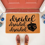 Hanukkah dreidel doormat featuring festive holiday text and a spinning top icon on natural coir fiber, perfect for a seasonal front porch welcome mat entry decor that celebrates the winter festival of lights with a fun, modern