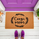 Corgi Mom doormat featuring a natural coir welcome mat with black script text and a leaf wreath design, placed on a white porch in front of a purple door for a stylish dog lover home entrance decor look.