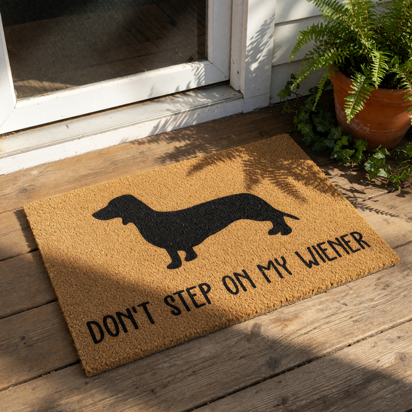 Dachshund doormat featuring a black silhouette of a wiener dog on natural coir fiber, with the funny text Don't Step On My Wiener printed below, making this a humorous outdoor welcome mat for any dog lover home entrance.