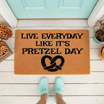 Pretzel Day doormat featuring funny food quote text and a large pretzel icon, this natural coir welcome mat is a durable outdoor floor rug for your front porch entry, perfect for snack lovers and home decor enthusiasts alike.