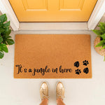It's a jungle in here doormat with paw prints and leaf designs, a natural coir fiber welcome mat for pet owners placed at a yellow front door, perfect for a house with dogs or cats and indoor plants for a fun entryway decor look.