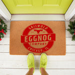 Holiday coir doormat featuring a red circular logo with moose antlers and text about an eggnog company in Chicago, placed on a porch with festive greenery for a fun Christmas welcome mat decor look for your front door entrance.