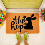 Easter bunny doormat featuring a black rabbit silhouette and the text Hip Hop on a natural coir welcome mat, styled on a front porch with colorful eggs and spring flowers for a festive seasonal home entryway decor look.