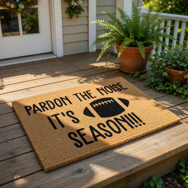 Football season doormat with Pardon the Noise text and a black football graphic, this natural coir fiber welcome mat is a funny sports decor piece for your front porch entrance during the fall game day season for any football fan