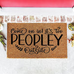 Funny doormat with the text Come on in it is too peopley outside, this natural coir fiber welcome mat features bold black lettering and decorative leaf accents for a stylish front porch decor piece for your home entrance.