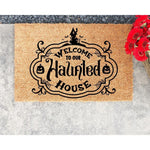 Haunted house welcome doormat with spooky Halloween decor, featuring a black printed design on natural coir fiber.
