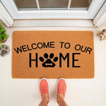 Dog paw print welcome doormat for pet lovers, featuring a natural coir fiber texture and black text that reads Welcome to our home with a paw print replacing the letter O, perfect for a front porch entryway or housewarming decor.