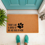Funny dog doormat with paw print design and text reading There's Like A Bunch Of Big Ass Dogs In Here, featuring a natural coir fiber welcome mat placed on a porch for pet owners who love humorous home decor and dog lover gifts.