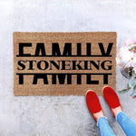Personalized family name coir doormat featuring bold black text on a natural fiber welcome mat, perfect for a custom housewarming entry rug or front porch decor, shown on a concrete floor with red shoes and floral accents nearby.