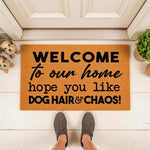 Funny dog hair and chaos welcome doormat for pet lovers, featuring a natural coir fiber texture with bold black text, placed on a front porch with small dog figurines and a person wearing gray sneakers standing on the entry mat.