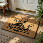 Personalized bowling doormat featuring a black bowling ball and pins graphic on a natural coir fiber welcome mat, perfect for a bowling enthusiast home entrance or front porch decor with custom family name text printed in black