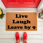 Funny doormat with the text Live Laugh Leave by 9, a natural coir welcome mat for front porch decor that makes a humorous housewarming gift for guests, shown on a white wood porch with red shoes standing on the mat in front of a