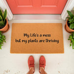 Funny plant lover doormat with the text My Life's a mess but my plants are thriving, featuring a natural coir fiber welcome mat design for a front porch entrance, perfect for housewarming decor or a unique home entryway floor rug.