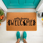 Every Bunny Welcome coir doormat for spring porch decor, featuring a cute rabbit silhouette and black script text on a natural fiber welcome mat, perfect for a seasonal front door entrance with a basket of carrots nearby.