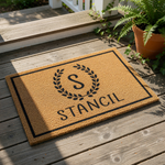Personalized monogram doormat with a natural coir fiber texture, featuring a black laurel wreath design around a custom initial and family name, making a stylish front porch welcome mat for housewarming or home decor entryways.