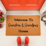 Grandma and Grandpa welcome doormat featuring natural coir fiber, placed at a front door entrance with red shoes visible, making a personalized housewarming floor mat for grandparents and family home decor entryways.