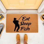 Fishing doormat with Eat Sleep Fish text and a fisherman silhouette on natural coir fiber, a funny outdoor welcome mat for anglers, cabin decor, or a front porch entrance rug for fishing enthusiasts who love outdoor hobbies.