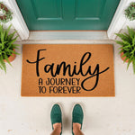 Family A Journey To Forever coir doormat featuring black script text on a natural fiber welcome mat, placed on a front porch entryway with green plants and shoes visible, perfect for a housewarming gift or home decor entrance rug.
