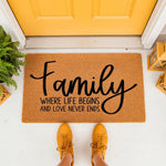 Family quote doormat for front porch entry, featuring a natural coir welcome mat with black script text that reads Family Where Life Begins And Love Never Ends, placed on a white floor by a yellow door for a stylish home decor