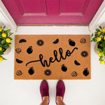 Hello lemon doormat with a natural coir fiber texture and black printed fruit pattern, placed at a bright pink front door entrance with potted lemon trees, perfect for a stylish summer porch decor or a housewarming welcome mat.