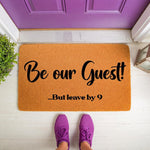 Funny welcome doormat with the text Be our Guest but leave by 9, featuring a natural coir fiber texture on a front porch.