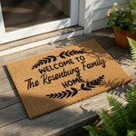 Personalized family name doormat featuring a natural coir fiber texture with black printed text that reads Welcome to the family home, accented by decorative leaf branches for a stylish farmhouse porch decor entryway mat.