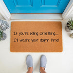 Funny doormat with text If you are selling something I will waste your damn time, a natural fiber coir welcome mat for front porch decor, featuring a humorous message for solicitors placed outside a bright blue door on a white