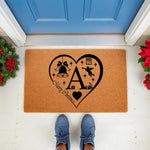 Personalized Christmas doormat featuring a large heart design with a central letter, holiday bell, and festive icons on a natural coir welcome mat, perfect for seasonal front porch decor and entryway floor mats for the winter