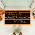 Horror movie quote doormat featuring black and orange stripes with text that reads One Two Freddy's Coming For You, perfect for a spooky Halloween porch decor setup with pumpkins and a skull on a front entryway floor mat.