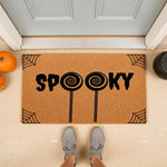Spooky Halloween doormat with lollipop design on natural coir fiber, featuring spider web corners and a festive fall porch setting.