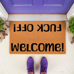 Funny welcome doormat with rude text in black lettering on a natural coir fiber mat, placed on a porch in front of a purple door with purple shoes visible, making this a perfect sarcastic housewarming decor item for your front