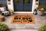 At least my dog loves me doormat featuring paw prints and a heart design on a natural coir fiber welcome mat, displayed on a stone porch as a funny pet lover front door rug for dog owners who want a humorous home entrance decor