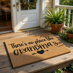Grandma doormat with a natural fiber texture, featuring the text There is no place like Grandma's and a heart arrow design, displayed on a front porch as a decorative welcome mat for a home entrance or housewarming decor.